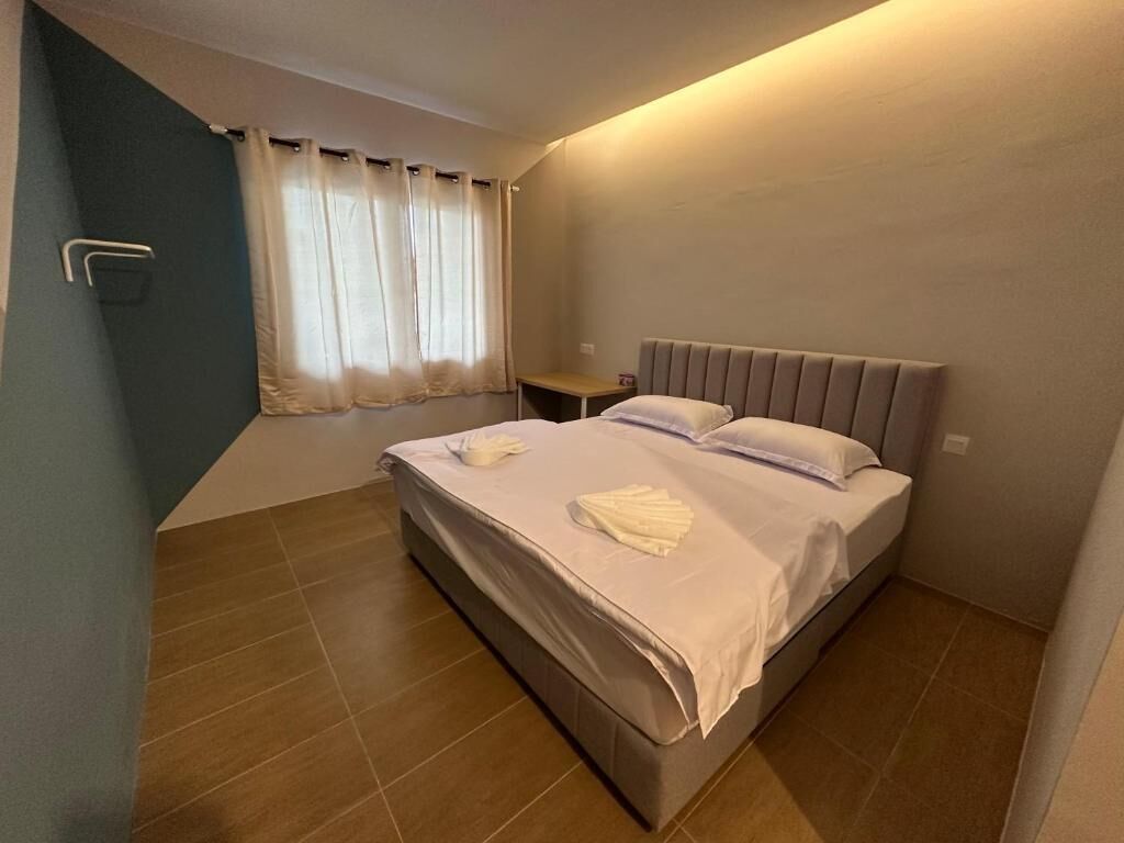 Un dormitorio con cama, mesita de noche y ventana con cortinas.