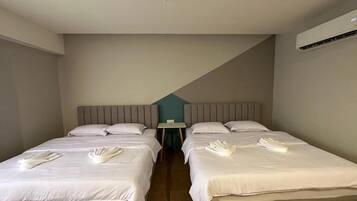 Quarto de hotel com duas camas, uma mesa pequena e um ar condicionado.