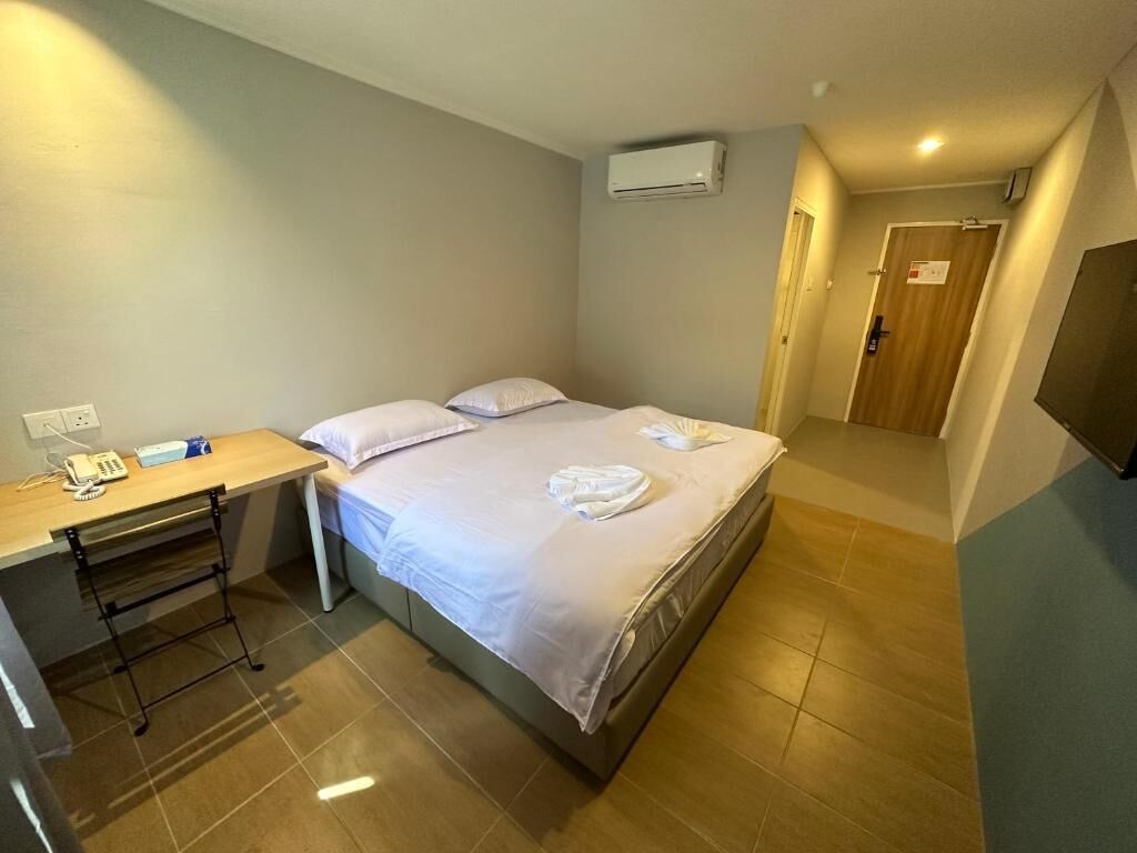 A hotel room with a bed, a desk with a telephone, and an air conditioning unit on the wall.