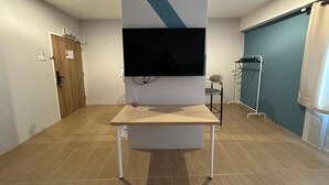 Una habitación con una televisión montada, una mesa de madera, una puerta y una pared azul.