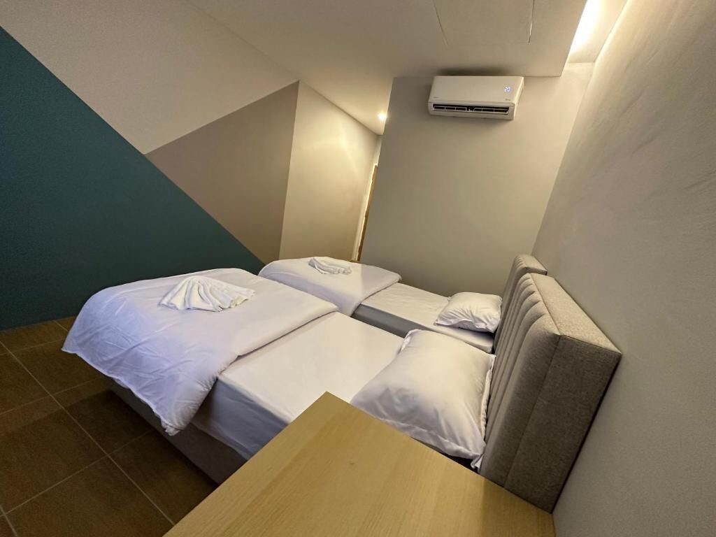 Habitación de hotel pequeña y funcional con una cama individual, una mesa de madera y un aire acondicionado en la pared.