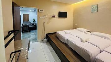 A hotel room with two beds, a TV mounted on the wall, and a desk with a chair.