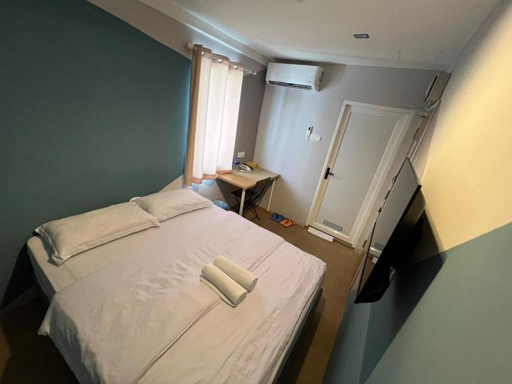 Quarto pequeno e bem organizado, com cama, escrivaninha e aparelho de ar condicionado.