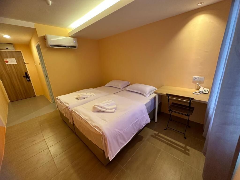 A hotel room with a bed, a desk, and an air conditioning unit.