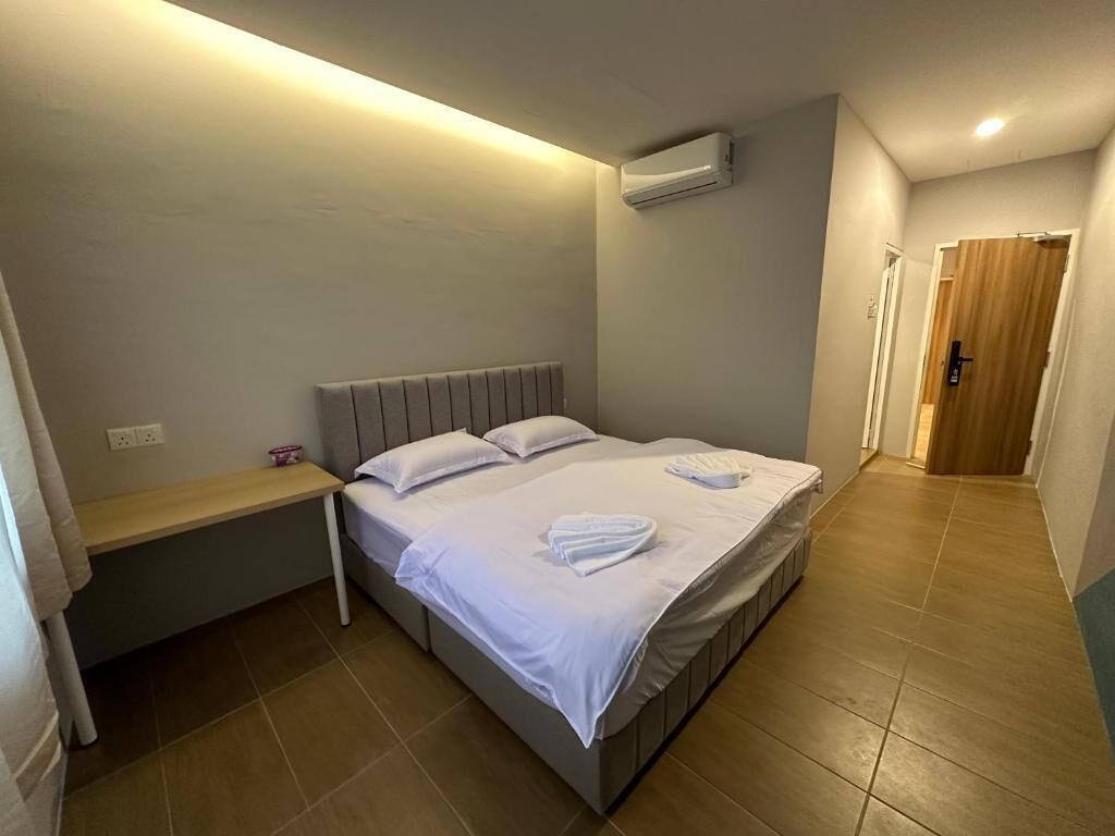 Una cama individual con ropa de cama blanca y dos toallas, una mesita de noche y un equipo de aire acondicionado en la pared.