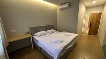 Una cama individual con ropa de cama blanca y dos toallas, una mesita de noche y un equipo de aire acondicionado en la pared.