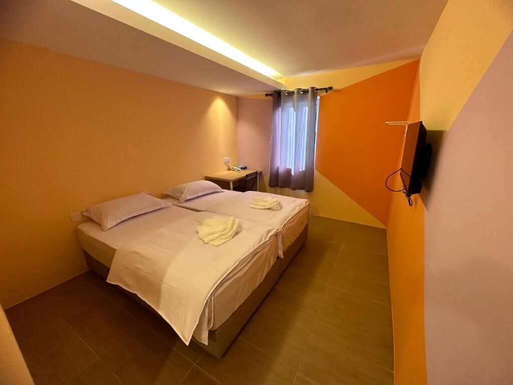 A hotel room with two beds, a desk, a chair, a TV, and a window with curtains.
