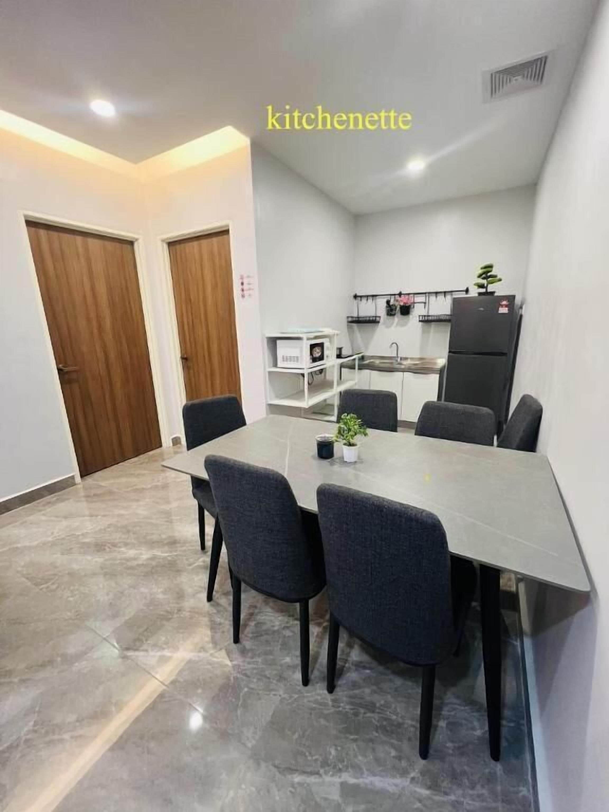 Una kitchenette moderna con zona de comedor, que presenta suelo de mármol, sillas grises y un lavamanos empotrado.