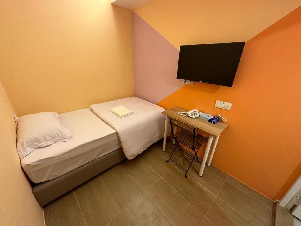 A small room with a bed, a desk with a telephone, and a television mounted on the wall.