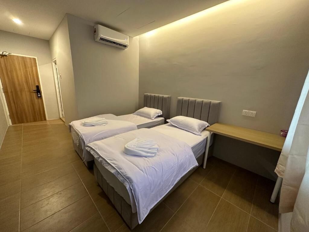 A hotel room with two beds, a wooden door, an air conditioning unit, and a small wooden bench.