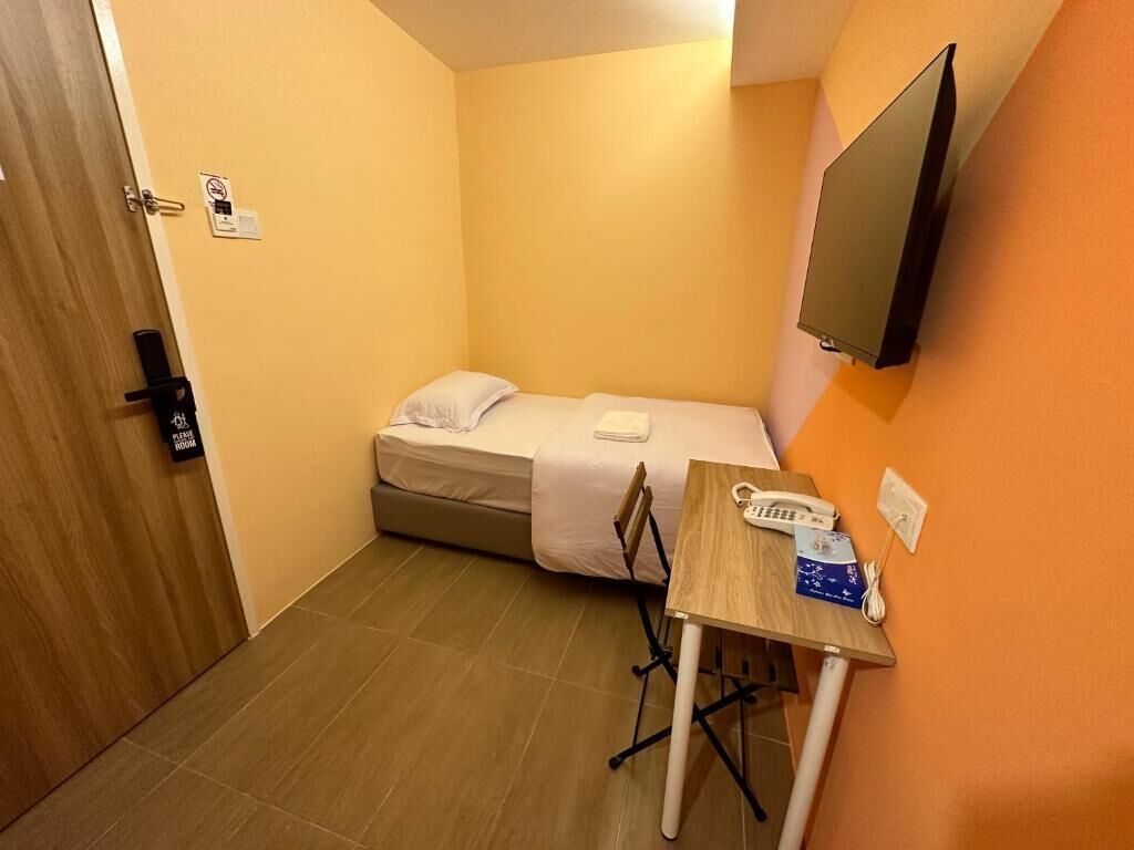 A small room with a bed, a desk, a chair, a phone, and a TV mounted on the wall.