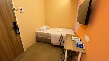 A small room with a bed, a desk, a chair, a phone, and a TV mounted on the wall.