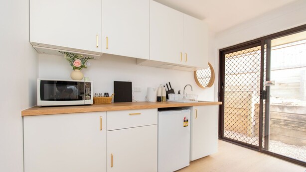 Una cocina moderna con armarios blancos, un microondas, un refrigerador pequeño y una encimera de madera.
