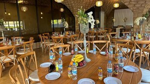 Un comedor amplio con mesas redondas de madera, sillas y diferentes tipos de vajilla, incluyendo platos, cubiertos y botellas de agua.