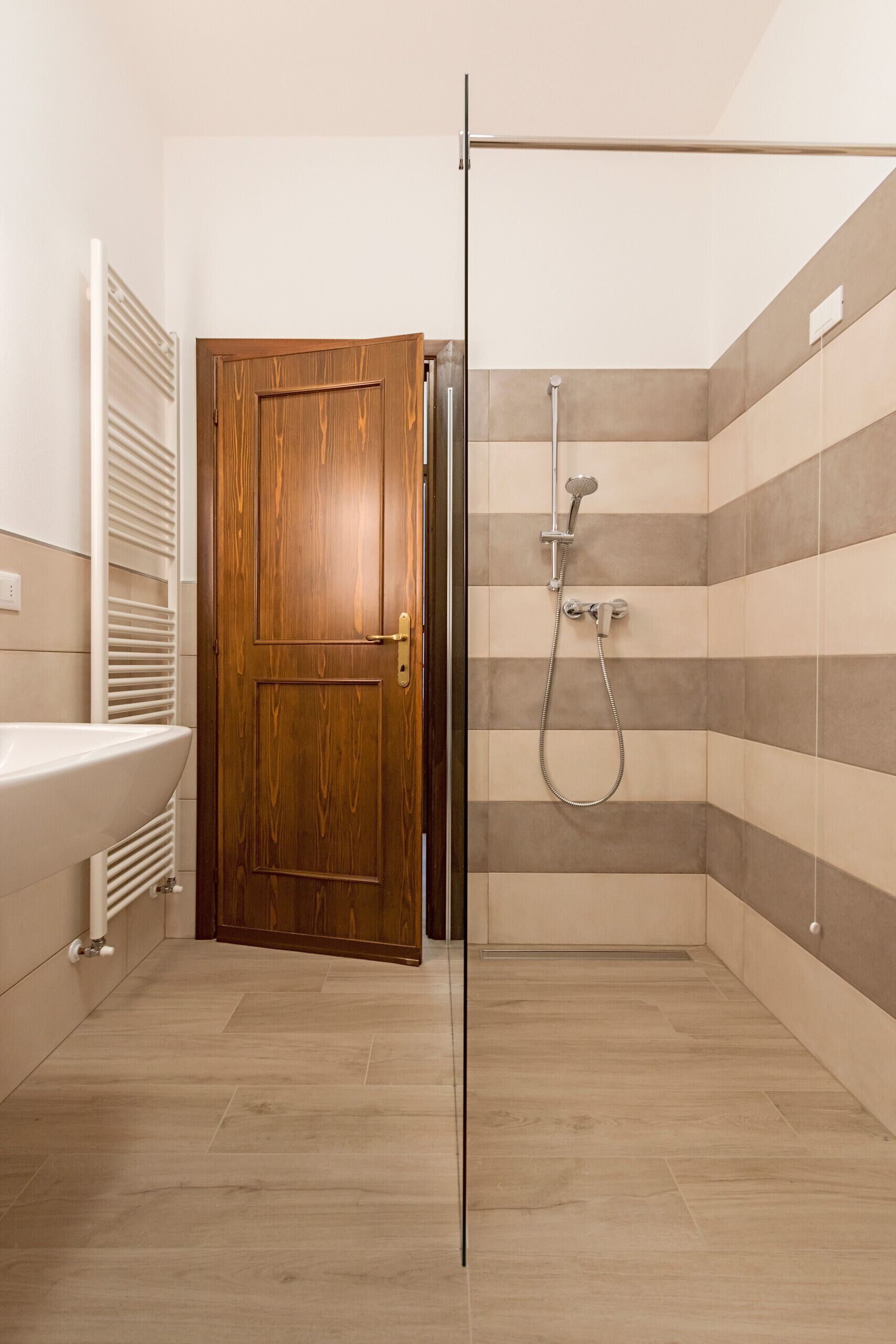Une salle de bain avec une porte en bois, une douche équipée d’un pommeau de douche à main et un lavabo blanc.