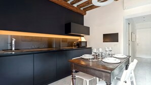 A modern kitchen with dark cabinetry, a wooden dining table set with plates and glasses, and a TV mounted on the wall. - Dimora San Lorenzo – Central Venice 2BR with Private Courtyard (Venezia)