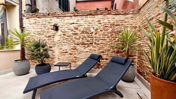A sunlit outdoor seating area with two lounge chairs, a small table, and potted plants against a stone wall. - Dimora San Lorenzo – Central Venice 2BR with Private Courtyard (Venezia)