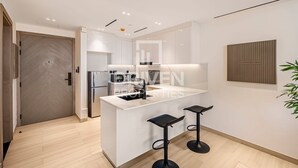 A modern kitchen with white cabinetry, a central island with stools, a built-in oven, and a microwave. - Cozy 1-bedroom apartment in Dubai (Dubai)