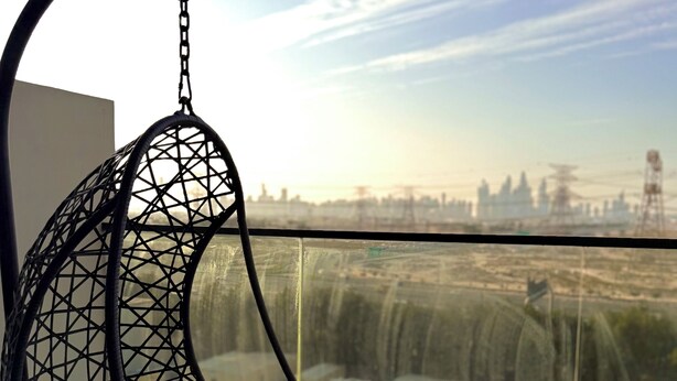 A black hanging chair with a cushion, a small black table, and a view of a cityscape through a glass railing. - Cozy 1-bedroom apartment in Dubai (Dubai)