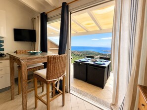 A dining area with a table and chairs, a television, and a view of the sea. - L' Ancora - Key to Villas (Paduledda)