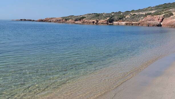 En vacker strand med stilla vatten, en sandstrand och bergiga kullar i bakgrunden.