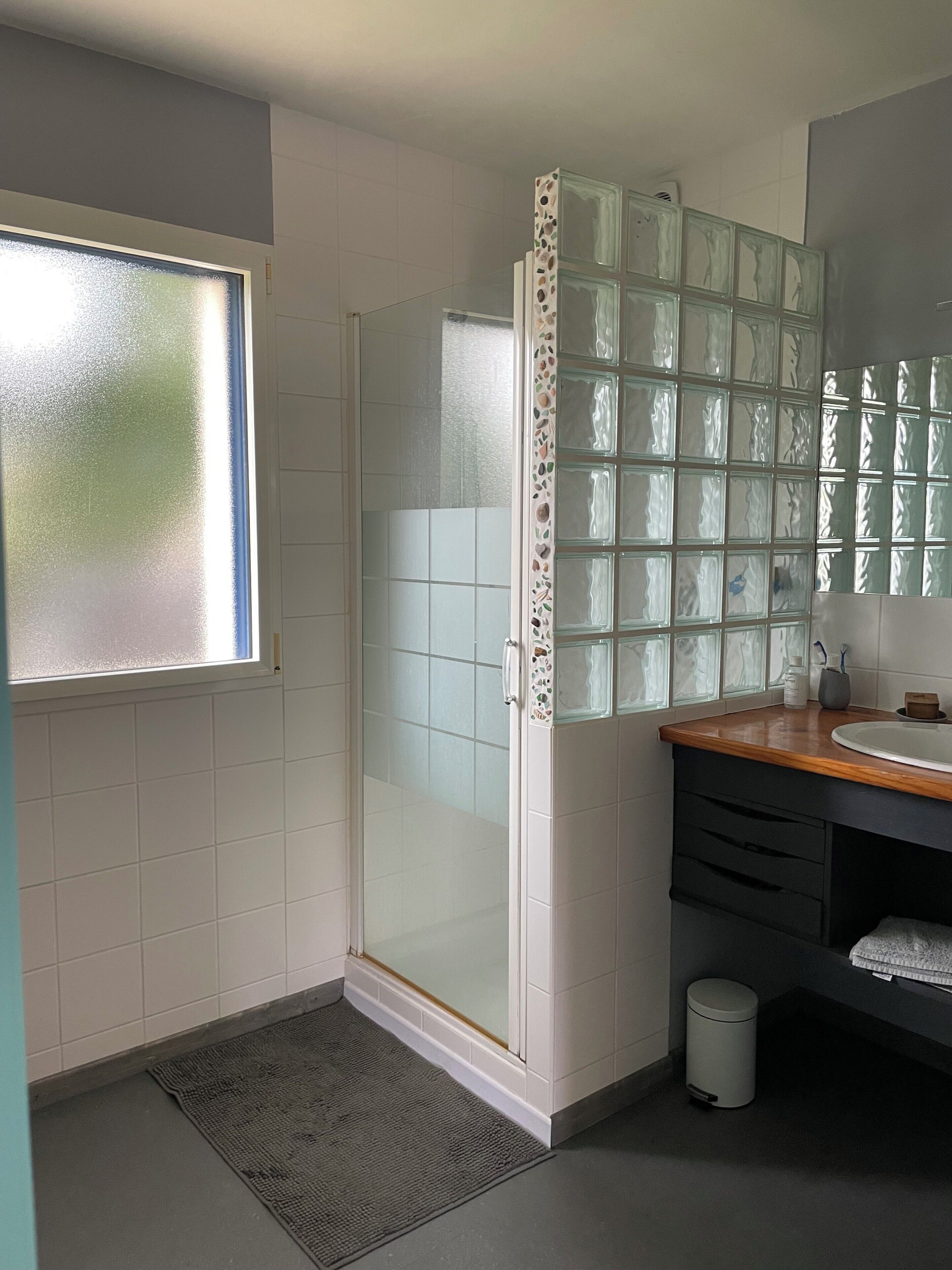 A bathroom with a glass shower enclosure, a sink with a wooden countertop, and a mirror with a mosaic border.