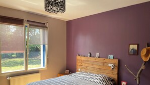 Een slaapkamer met een bed, een dressoir, een raam met jaloezieën en een wandlamp.