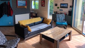 Een moderne woonkamer met een bank, een salontafel en een stoel. Er zijn ramen, een radiator en een tv aan de muur bevestigd.