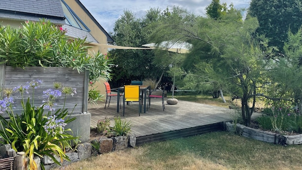 Een terras met houten vlonder, tuinmeubilair en diverse planten.