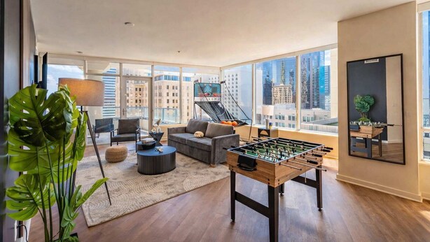 A modern living room with a foosball table, comfortable seating, a large window with a city view, and a staircase. - Downtown PHX Retreat Pool, Gym Balcony Views (Phoenix)
