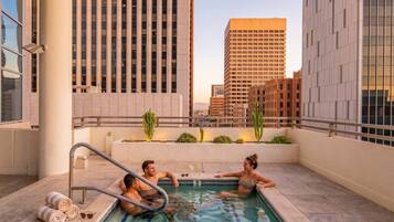 A rooftop pool area with three people, a pool, and a view of surrounding buildings.