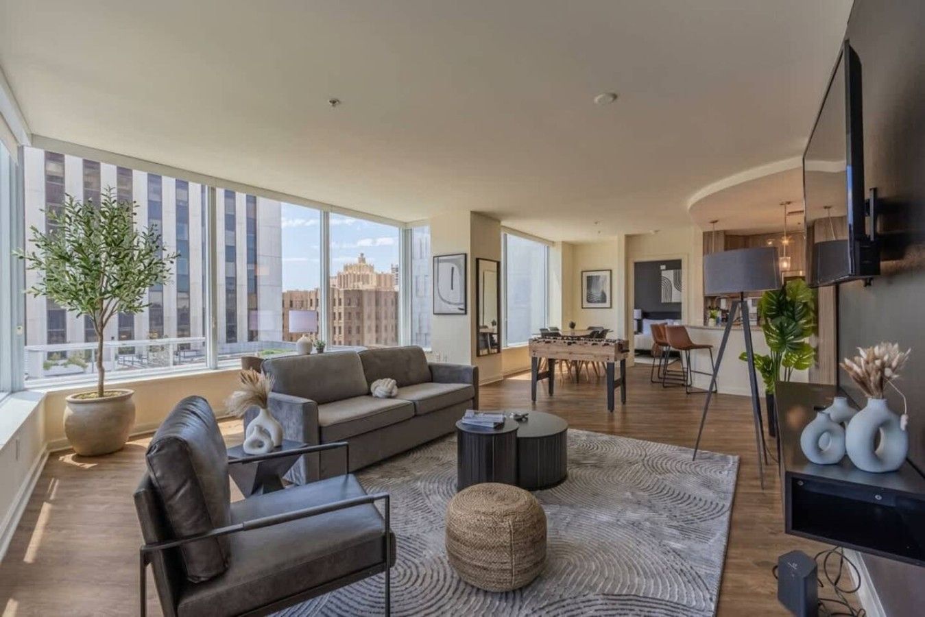 A spacious living area with a sofa, coffee table, and ottoman, a dining area with chairs, and a kitchen in the background.