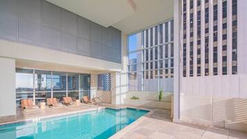 An indoor swimming pool with lounge chairs and a view of a cityscape through large windows.