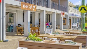 An outdoor cafe with wooden tables and chairs, a sign for 'Room Cafe', and a 'Bada Sushi' restaurant in the background. - Flynns Beach Seascape (Port Macquarie)