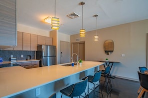 A modern kitchen with a central island, bar stools, pendant lighting, and a large mirror. - Modern ASU Apt | Roosevelt Row | W/D + FreeParking (Phoenix)
