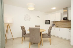 Eine moderne Küche mit weißen Schränken, einem runden Holztisch und vier grau gepolsterten Stühlen.