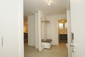 Ein modernes, minimalistisches Hotelzimmer mit integrierter Sitzbank, einem kleinen Tisch und einem separaten Duschbereich.