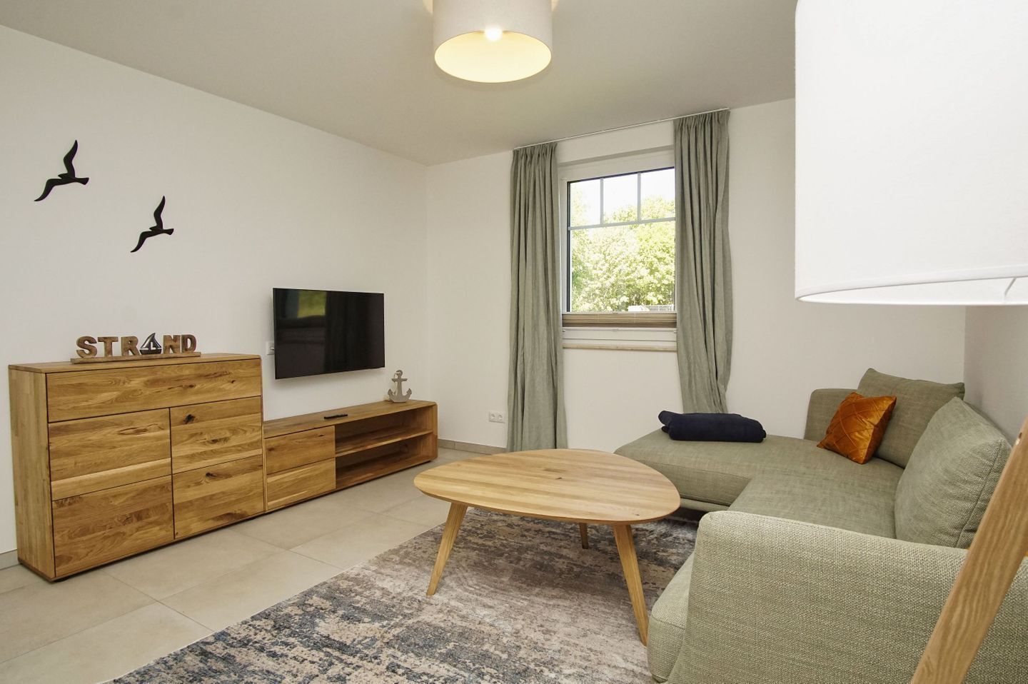 Una sala de estar moderna con un mueble de madera, un televisor de pantalla plana, una mesa de centro redonda de madera y un sofá verde con cojines.