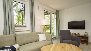 Ein Wohnzimmer mit Sofa, Sessel, Couchtisch, Fernseher und Lampe.
