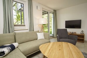 A living room with a sofa, a chair, a coffee table, a TV, and a lamp. - Beachfront apartment with terrace - Rex Rugia House 17 Apartment 03 - Beach Resort (Mönchgut)