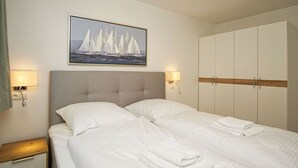 Ein Hotelzimmer mit einem Bett, zwei Nachttischlampen, einem Segelbootgemälde und einem Kleiderschrank.
