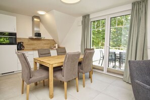A modern kitchen with a wooden table and chairs, a built-in oven, and a large sliding glass door leading to an outdoor area. - Beachfront apartment with balcony - Rex Rugia House 17 Apartment 05 - Beach Resort (Mönchgut)