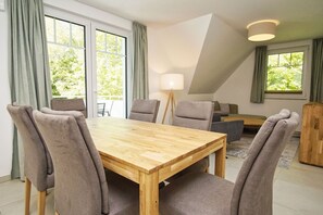 A dining area with a wooden table and chairs, a lamp, and a sofa in the background. - Beachfront apartment with balcony - Rex Rugia House 17 Apartment 05 - Beach Resort (Mönchgut)
