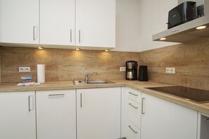A modern kitchen with white cabinets, a wooden countertop, a stainless steel sink, and a coffee maker. - Beachfront apartment with balcony - Rex Rugia House 17 Apartment 08 - Beach resort (Mönchgut)
