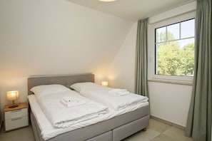 Ein Schlafzimmer mit zwei Betten, einem Nachttisch, einer Lampe und einem Fenster mit Vorhängen.