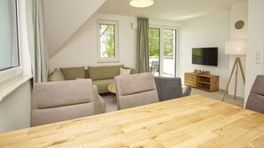 Una sala de estar moderna con una mesa de comedor de madera, sofás grises y un televisor en la pared.