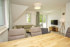 Ein modernes Wohnzimmer mit einem Holzespeisetisch, grauen Sofas und einem Fernseher an der Wand.