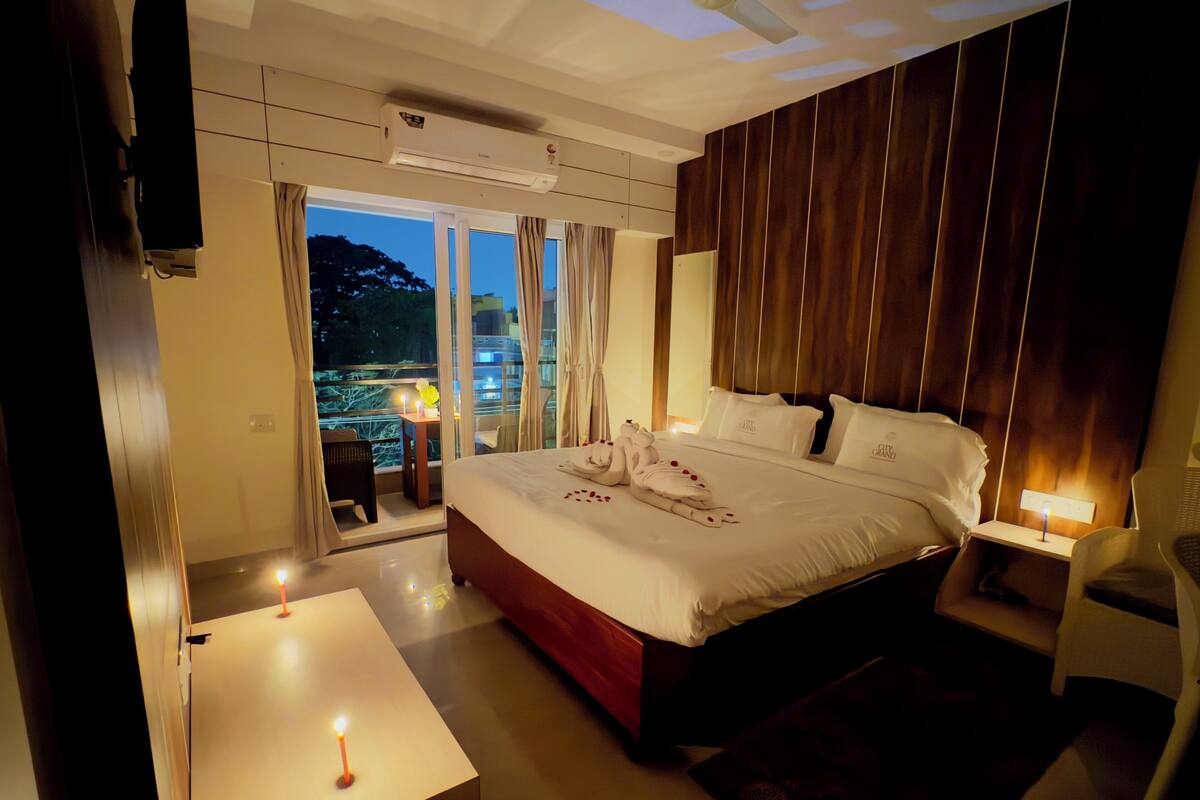 A hotel room with a large bed, a balcony with a table and chairs, and a view of the cityscape.