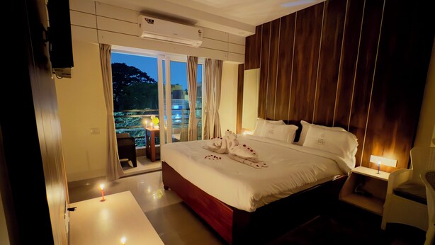 A hotel room with a large bed, a balcony with a table and chairs, and a view of the cityscape. - CITY GRAND (Puri)