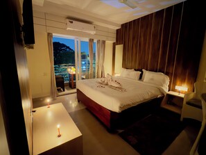 Quarto de hotel com uma cama grande, varanda com mesa e cadeiras, e vista para a cidade.